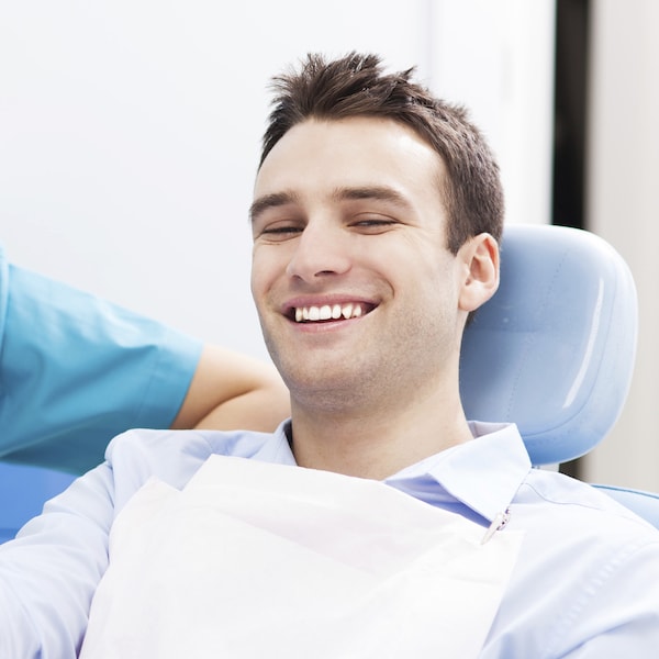 Young man sitting in a blue dental treatment chair smiling with his restorative dentist