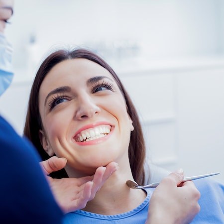 A close up of a woman in a dental chair smiling while her family dentist holds up a dental mirror